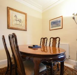 A dining room with wooden table and chairs two framed pictures on walls and a floor lamp at Sunnybrae Alnmouth