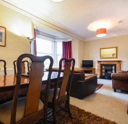 A dining area with wooden chairs and table next to a living room with leather sofas a fireplace and a television at Sunnybrae Alnmouth