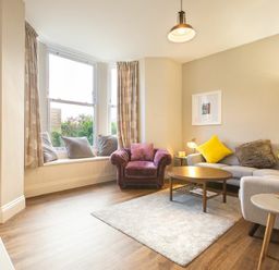 A living room with a gray sofa with yellow cushions a purple armchair a coffee table and a window seat with cushions at Sandybrae in Alnmouth