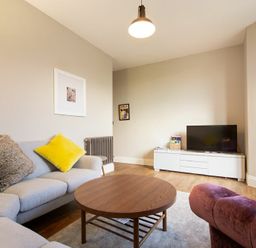 A living room with a gray sofa with cushions a round wooden coffee table a white TV stand and a flat screen TV at Sandybrae in Alnmouth