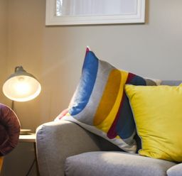A corner of a living room with a gray sofa featuring colorful cushions and a lit table lamp on a side table at Sandybrae in Alnmouth