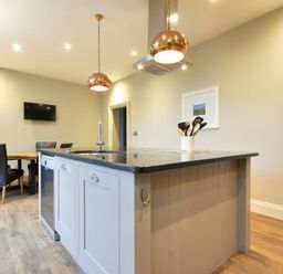 A kitchen with an island counter having a sink and utensils beside a dining table with chairs at Sandybrae in Alnmouth