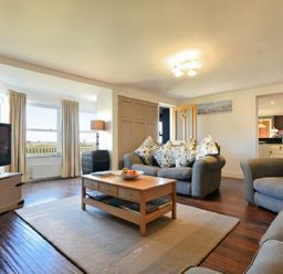 A living room with three armchairs a wooden coffee table a television and large windows at Mariners House in Alnmouth