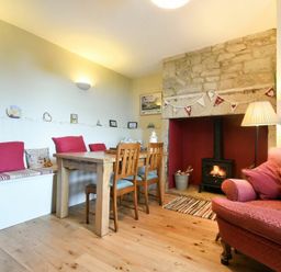 A dining area with a wooden table and chairs next to a fireplace and a pink sofa at Farne View Cottage in Seahouses