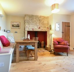 A dining area with wooden table and chairs next to a stone fireplace and an armchair at Farne View Cottage in Seahouses