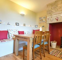 A dining area with a wooden table and chairs bench seating with cushions and a stone fireplace at Farne View Cottage in Seahouses