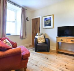A sitting room with a red sofa a leather armchair a wooden TV stand with a television and a framed picture on the wall at Farne View Cottage in Seahouses