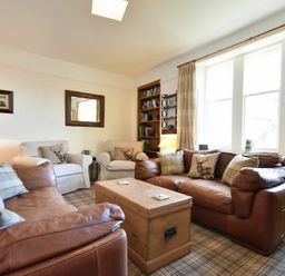 A living room with brown leather sofas beige armchairs wooden chest and bookshelf at Whistlewood in Bamburgh