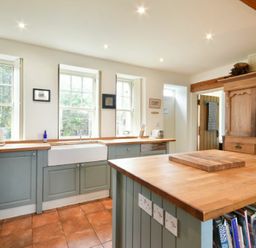 A kitchen with blue cabinets wooden countertops a large wooden island and three windows at Whistlewood in Bamburgh