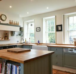 A kitchen with wooden countertops a kitchen island cookbooks and three windows at Whistlewood in Bamburgh
