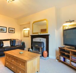 A living room with a black sofa cushions wooden coffee table fireplace and a television on a wooden stand at Castle View Warkworth