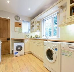 A kitchen with white cabinets wooden countertops a washing machine dishwasher and window at Castle View Warkworth