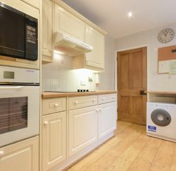 A kitchen with cream cabinets wooden countertops oven microwave washing machine and a wooden door at Castle View Warkworth