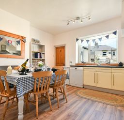 A kitchen with a dining table and six wooden chairs next to a window with bunting at Rosedale House in Amble