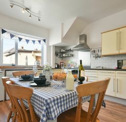 A kitchen with a wooden dining table covered with a blue checkered tablecloth and wooden chairs at Rosedale House in Amble