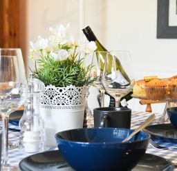 A dining table set with blue bowls black mugs wine glasses a white decorative flower pot and muffins on a cake stand at Rosedale House in Amble
