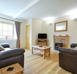 A living room with two leather sofas a wooden coffee table a TV on a wooden stand a fireplace and a window with curtains at Dryden Cottage in Bamburgh