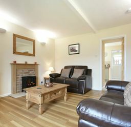 A living room with brown leather sofas a wooden coffee table a fireplace and a television at Dryden Cottage in Bamburgh