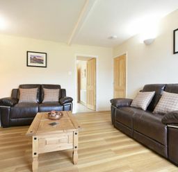 A living room with two brown leather sofas wooden coffee table wooden side table and framed pictures on walls at Dryden Cottage Bamburgh