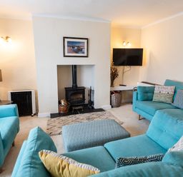 A living room with turquoise sofas a patterned ottoman a wood-burning stove and a wall-mounted TV at Percy Cottages No4 in Alnmouth