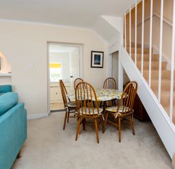 A dining area with a table and six chairs next to carpeted stairs and a blue sofa in a living room at Percy Cottages No4 in Alnmouth