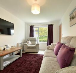 A living room with a beige sofa with purple cushions a beige armchair a wooden coffee table and a wall mounted television at The Chevy in Seahouses
