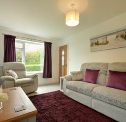 A living room with gray armchair sofa and purple cushions at The Chevy in Seahouses