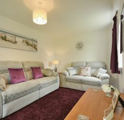 A living room with two grey sofas purple cushions and a wooden table at The Chevy in Seahouses