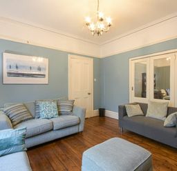 A living room with two sofas an ottoman wooden floor and blue walls at Nettie's View in Amble
