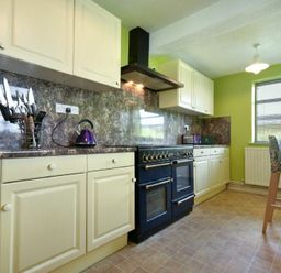A kitchen with cream cabinets a black stove a microwave and a wooden table with chairs at Nettie's View in Amble