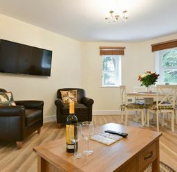 A living room with two black leather armchairs a mounted flat screen TV a wooden coffee table and a dining table with four chairs and flowers at The Lodge (Alnwick) in Alnwick