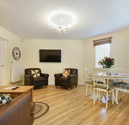 A living room with two brown armchairs a round dining table with four chairs and a mounted television at The Lodge (Alnwick) in Alnwick