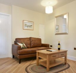 A living room with a brown leather sofa a wooden coffee table a bottle of wine a wine glass a framed picture and a wall mirror at The Lodge (Alnwick) in Alnwick