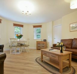 A living room with brown leather sofas a wooden coffee table a dining table with chairs and flowers at The Lodge (Alnwick) in Alnwick