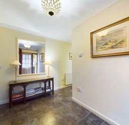A hallway with a large mirror above a wooden console table holding two lamps and books on a shelf at Rokeby in Bamburgh