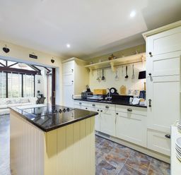 A kitchen with cream cabinets and black countertops next to a room with white sofas and large windows at Rokeby in Bamburgh