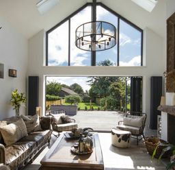A living room with large windows open to a garden a leather sofa armchairs a coffee table and a fireplace at Marmalade Cottage in Seahouses