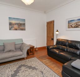A living room with two sofas a floor lamp wooden door and framed pictures on white walls at Anchor Cottage Seahouses