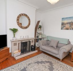 A living room with a fireplace a gray sofa a television and a decorative mirror at Anchor Cottage (Seahouses) in Seahouses