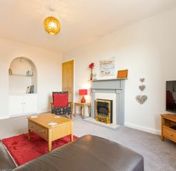 A living room with a fireplace a wooden coffee table a TV on a stand and armchairs at Church View in Bamburgh
