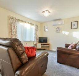 A living room with leather sofas a TV on a wooden stand a wall clock and framed pictures at Annstead House in Seahouses