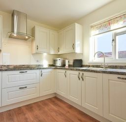 A kitchen with white cabinets a stainless steel oven hood a microwave sink under a window and a wooden floor at Annstead House in Seahouses