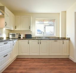A kitchen with white cabinets wooden floor a window a microwave oven and a sink at Annstead House in Seahouses