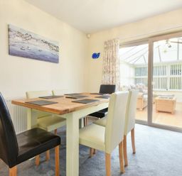 A dining room with wooden table and mixed color chairs next to sliding glass doors and floral curtains at Annstead House in Seahouses
