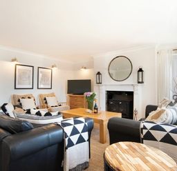 A living room with black leather sofas a wooden coffee table a fireplace with a round mirror and two lanterns at Cargoes in Craster