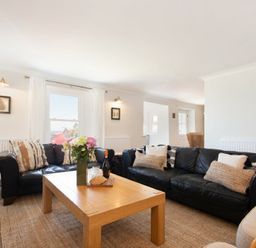 A living room with black sofas a wooden coffee table with flowers and food at Cargoes in Craster