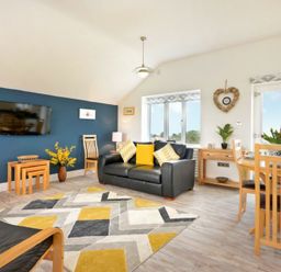 A living room with a black leather sofa with yellow pillows a geometric patterned rug and a blue accent wall with a mounted television at Viewpoint in Alnmouth