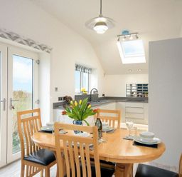A dining area with a wooden table set for four and a kitchen with white cabinets and a skylight at Viewpoint in Alnmouth