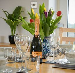 A dining table set with bowls plates wine glasses and a bottle of prosecco with a vase of tulips at Viewpoint in Alnmouth