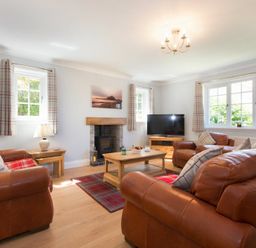 A living room with brown leather sofas, wooden coffee table, TV, fireplace, and windows with checked curtains at Castlewood in Bamburgh